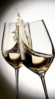 two wine glasses filled with white wine being poured into each other's beaks