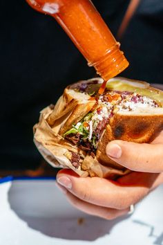 a person pouring ketchup onto a sandwich