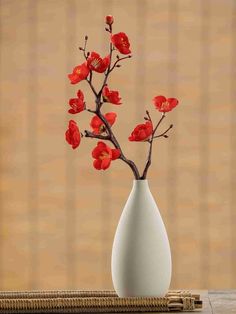 a white vase filled with red flowers sitting on top of a wooden table next to a bamboo mat