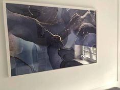 an abstract painting hangs on the wall next to a window in a room with white walls