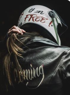 a woman wearing a leather jacket with a motorcycle helmet on her head and writing on the back