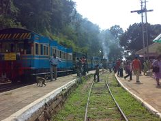 people are standing on the side of a train track as it pulls into a station