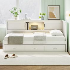 a white bed with drawers underneath it in a room next to a window and rugs on the floor