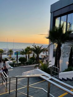 some people are walking up stairs near the beach at sunset or sunrise, with palm trees and buildings in the background