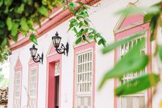 a pink and white building with two lamps on the outside, next to a tree