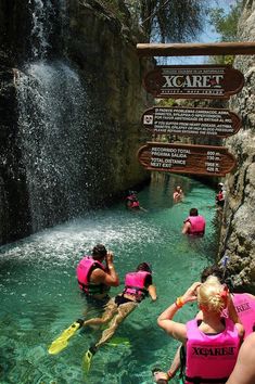 people in pink life vests are swimming near a waterfall