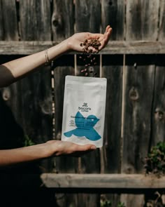 a person holding a bag of coffee beans in front of a wooden fence with a bird on it