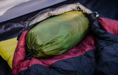 an open sleeping bag sitting on top of a black and red blanket next to a yellow pillow