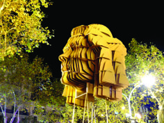 a large yellow sculpture sitting in the middle of a park at night with trees around it