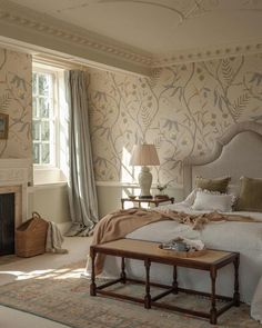 a bedroom with a bed, fireplace and window in the corner that has floral wallpaper on it