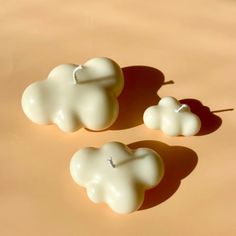 two small white candles sitting next to each other on a brown surface with one candle in the shape of a cloud