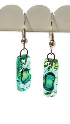 two green glass earrings hanging from hooks on a hook with metal earwires attached to them