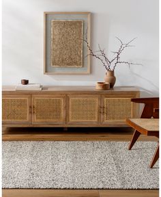 a room with a rug, chair and vase on the sideboard in front of it