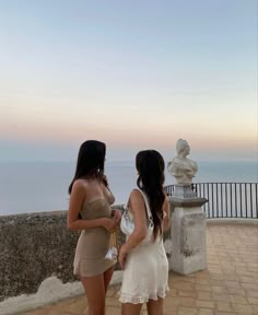 two young women standing next to each other on a balcony looking at the water and sky