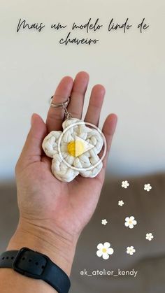 a hand holding a white and yellow brooch with a flower on it's center