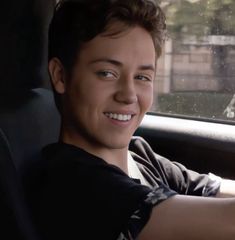 a smiling young man sitting in the driver's seat of a car