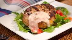 a white plate topped with meat covered in sauce and lettuce next to a fork