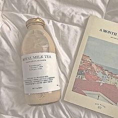 a bottle of tea sitting on top of a bed next to a book