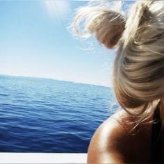 a woman looking out over the water from a boat on a sunny day with her hair in a bun