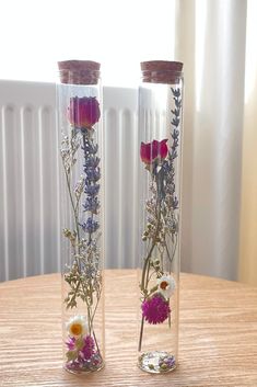 two clear vases with flowers inside sitting on a table