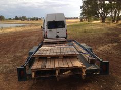 a white van is parked on the back of a flatbed trailer in an open field