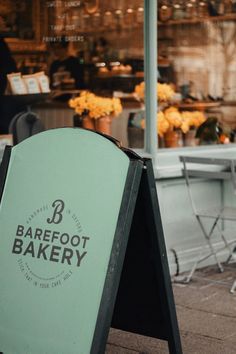 a green sign sitting on the sidewalk in front of a storefront that says barefoot bakery