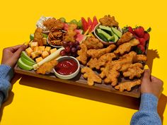 a person holding a platter full of food on top of a wooden tray with fruit and veggies