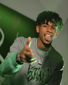 a young man with green paint on his face pointing at the camera while wearing a grey shirt