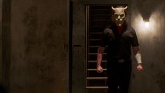 a man wearing a devil mask standing in front of a doorway