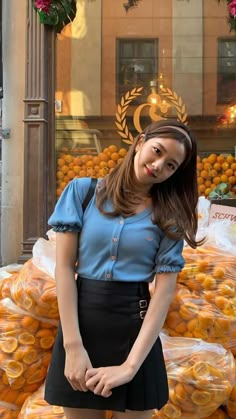 a woman standing in front of a pile of oranges with her hands on her hips