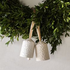 two white vases are hanging from a green wreath