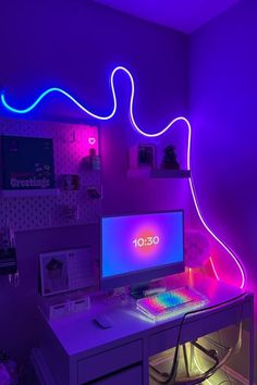 a desk with a computer and neon lights on the wall in a room that is lit up