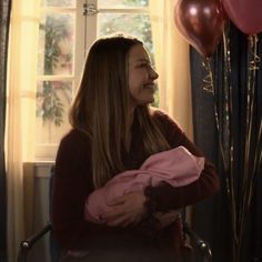 a woman sitting in a chair next to some red and pink balloons on a window sill