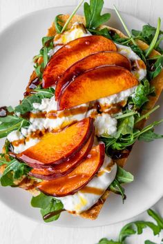 a white plate topped with sliced peaches and cheese on top of lettuce