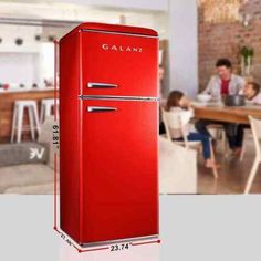 a red refrigerator sitting in the middle of a kitchen next to a family eating at a table