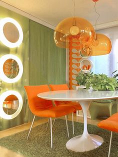 a dining room with green walls and orange chairs around a white table surrounded by plants