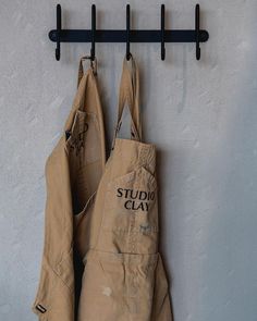 two aprons hanging on a wall with the words studio clay written on them and black hooks