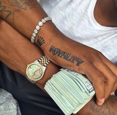 a man with tattoos on his arm and wrist holding stacks of money while wearing a watch