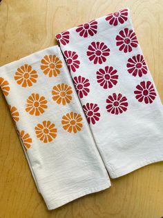 two white towels with orange and red flowers on them sitting on a wooden table next to each other