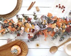 an arrangement of autumn leaves and pumpkins on a white wooden table with utensils