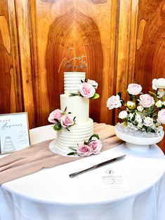 a white wedding cake sitting on top of a table next to flowers and a knife