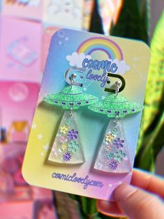 a pair of earrings is being held up in front of a card with the words cosmic land on it