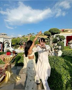 a man and woman walking down a walkway next to each other with their arms in the air