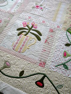 a close up of a quilt on a bed with pink and green flowers in the center