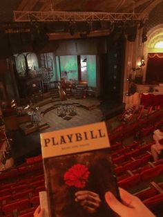 a person holding up a playbill book in front of an auditorium