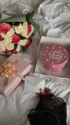 there is a pink birthday cake and flowers on the bed with it's box