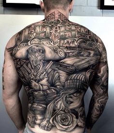 a man with tattoos on his back standing in front of a wall