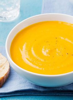 a white bowl filled with soup next to a slice of bread on a blue napkin