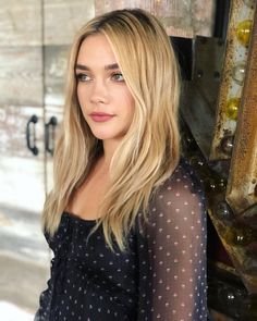 a woman with long blonde hair standing in front of a mirror and looking at the camera