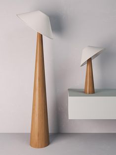 two wooden lamps sitting next to each other on top of a white shelf in front of a gray wall